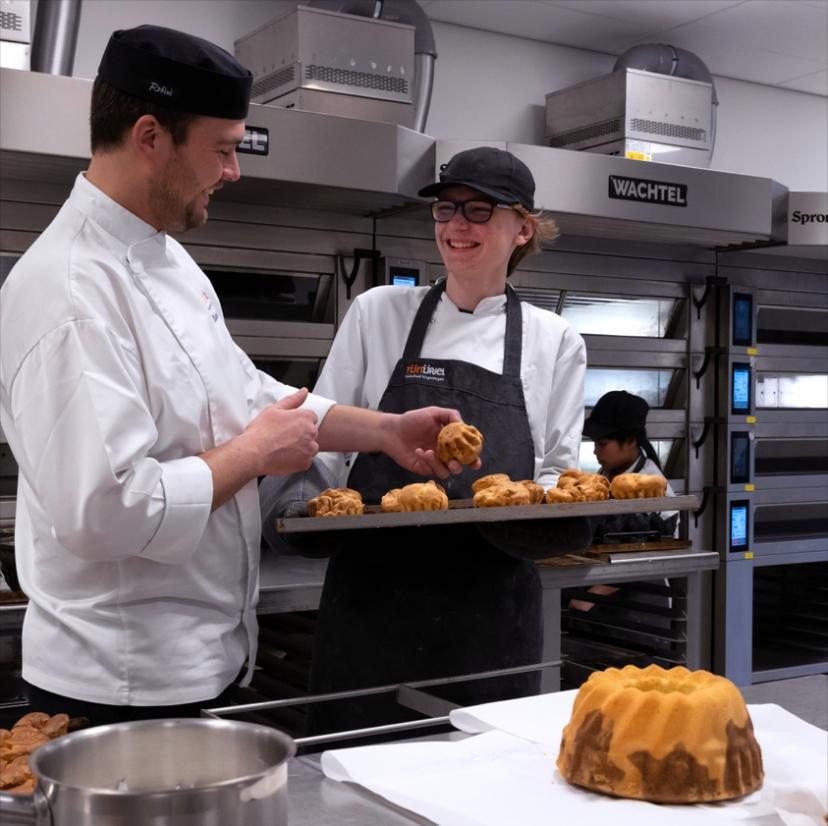 Bakkers in witte koksbuizen met vers gebakken producten in de opleidingskeuken